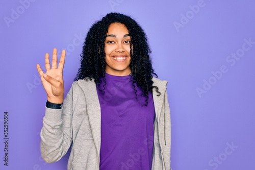 Young african american sporty woman wearing casual sweatshirt over purple background showing and pointing up with fingers number four while smiling confident and happy. © Krakenimages.com
