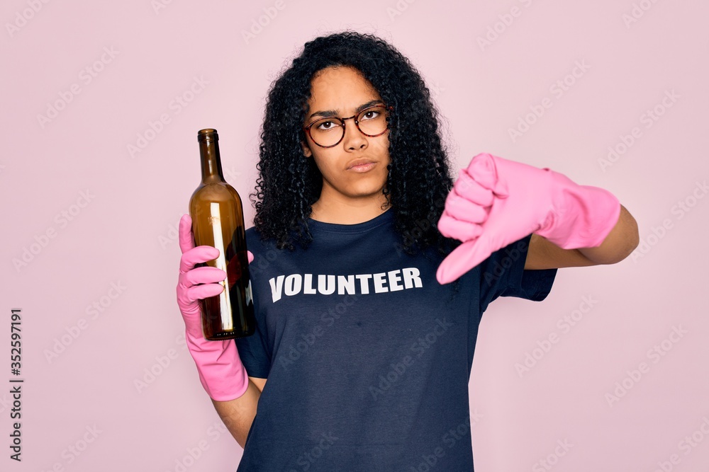 African american curly woman wearing volunteer t-shirt doing volunteering recycling glass bottle with angry face, negative sign showing dislike with thumbs down, rejection concept African american curly woman wearing volunteer t-shirt doing volunteering recycling glass bottle with angry face, negative sign showing dislike with thumbs down, rejection concept