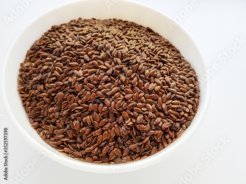 Flax seeds in a white ceramic plate on a white background.
