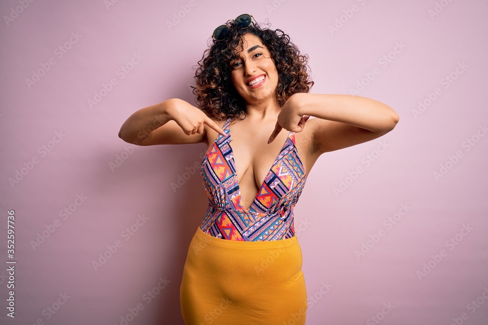 Young beautiful arab woman on vacation wearing swimsuit and sunglasses over pink background looking confident with smile on face, pointing oneself with fingers proud and happy. Young beautiful arab woman on vacation wearing swimsuit and sunglasses over pink background looking confident with smile on face, pointing oneself with fingers proud and happy.