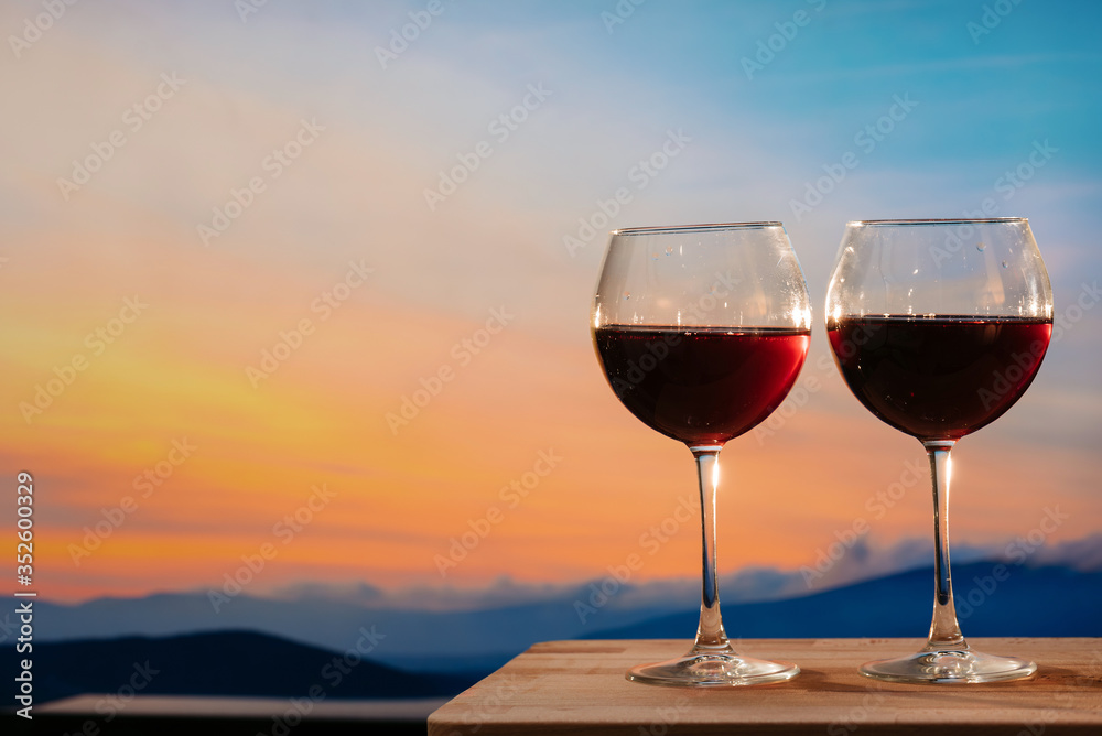 Glasses of red wine against sunset, red wine on the sky background with clouds