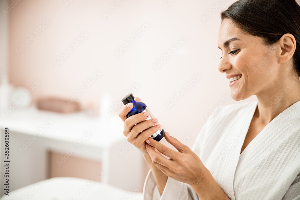 Cheerful pretty lady with bottle of cosmetics indoors Cheerful pretty lady with bottle of cosmetics indoors