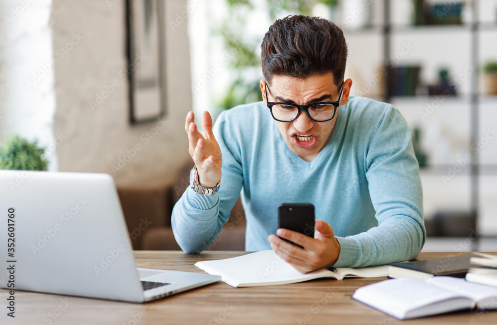 Angry ethnic freelancer reading message on smartphone.