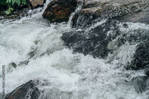 Full frame nature background of water riffle of mountain river. Powerful water stream of mountain creek with rapids. Natural textured backdrop of fast flow of mountain brook. Rapids texture close-up. © Daniil
