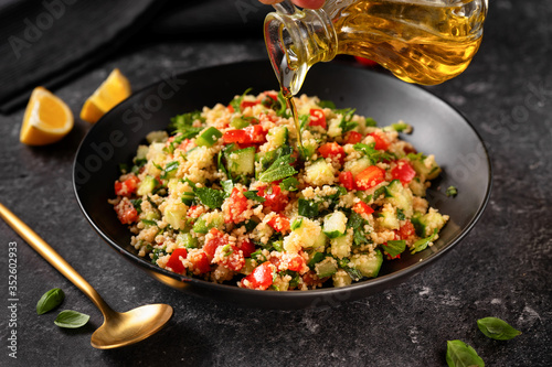 Pouring an olive oil into a plate with vegan fresh couscous salad