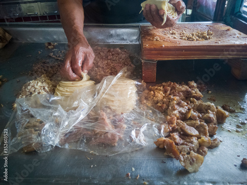 Elaboración de tacos tradicionales de diversos tipos de carnita, como barbacoa, oreja, sesos entre otros, se alcanza a ver las carnitas, la tabla de cortar carne y las manos de el taquero o cocinero. photo