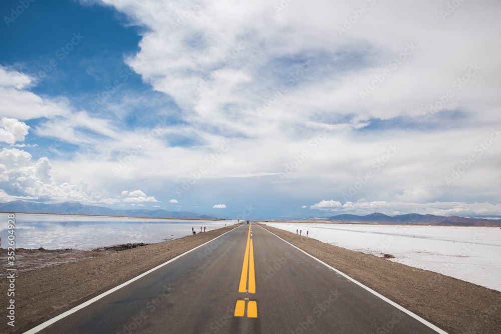 camino de asfalto en las salinas grandes en jujuy con nubes sobre cielo azul