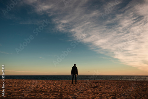 man with a hoddie looking at the sea from the beach