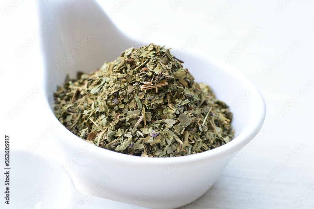 Chopped dried leaves of basil leaves on white wooden background Chopped dried leaves of basil leaves on white wooden background