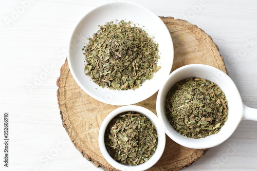 Chopped dried leaves of basil leaves on white wooden background