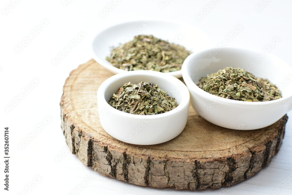 Chopped dried leaves of basil leaves on white wooden background