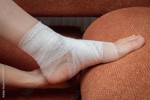 A young woman at home independently bandages her leg and lower leg with a bandage. Proper self-help with a bruised leg. Side view photo