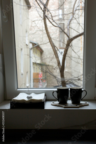 Two cups and a writing pad in front of the window, in the background is wood and buildings