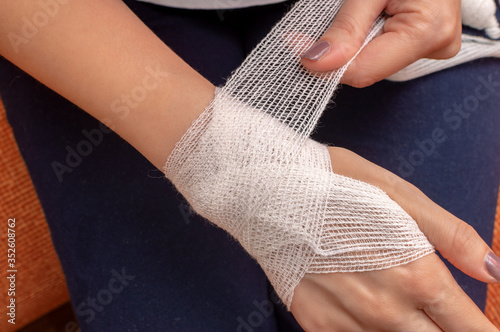 Young woman bandages her wrist independently. Close-up, top view, warm tinting.