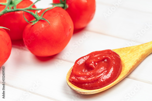 Tomato paste in wooden spoon with tomato on white background © Iana Alter