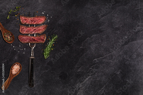 Grilled beef steak on black stone table. Top view with copy space