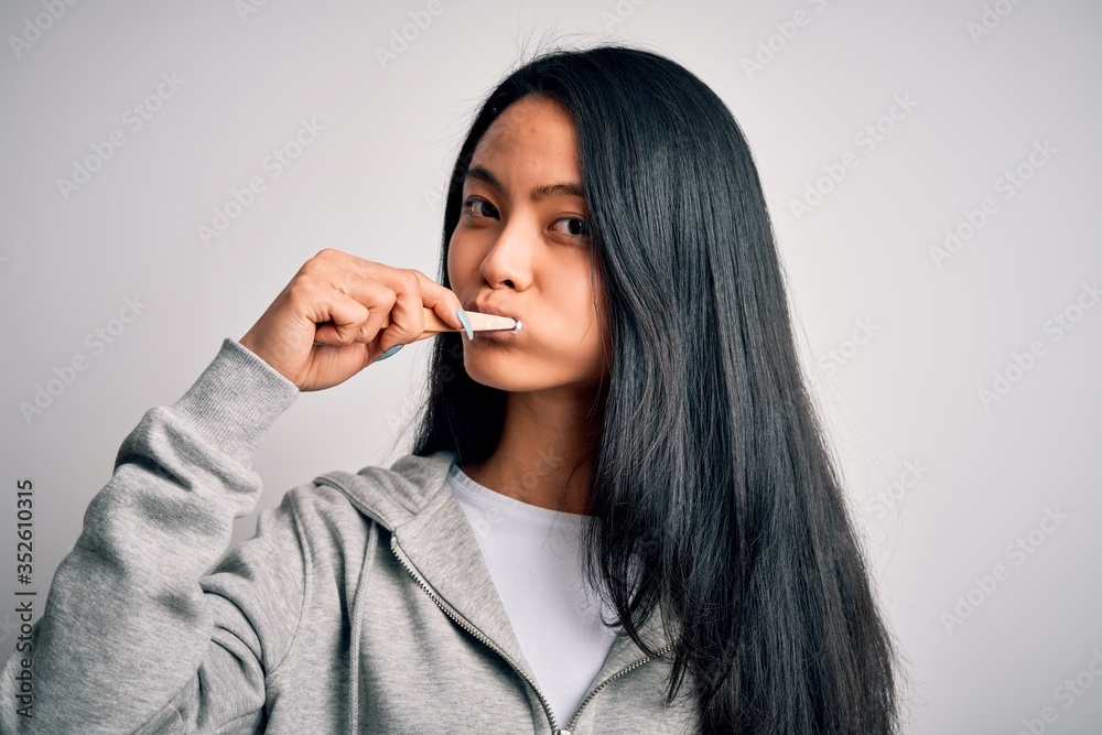 Young beautiful woman standing whasing tooth using toothbrush over isolated white background Young beautiful woman standing whasing tooth using toothbrush over isolated white background