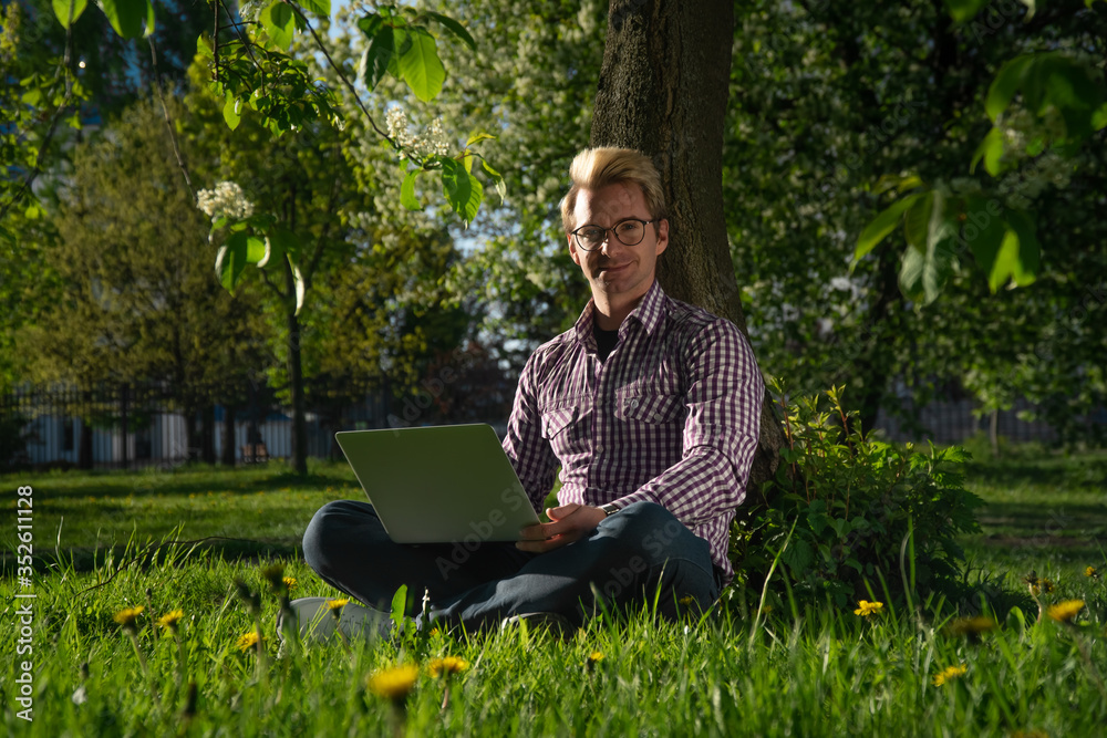 Headshot A young man freelancer is sitting under a tree on a sunny day. working on a laptop. Headshot A young man freelancer is sitting under a tree on a sunny day. working on a laptop.