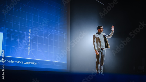 On-Stage Speaker Greets Audience, Presentation of Technological Device, Shows Statistics Infographics Animation on Screen. Auditorium Hall Live Event, Product Release, Start-up Conference. © Gorodenkoff