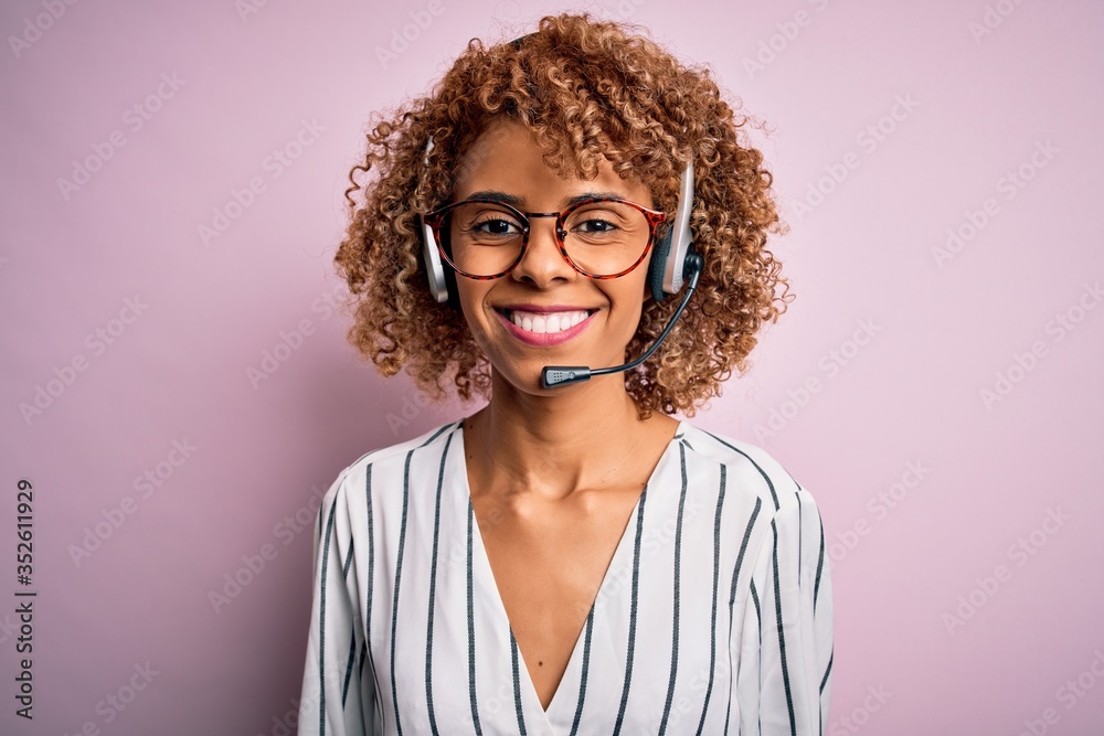 African american curly call center agent woman working using headset over pink background with a happy and cool smile on face. Lucky person.