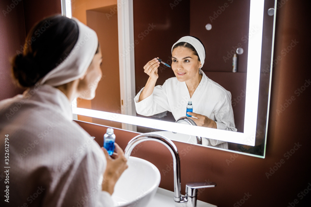 Smiling lady applying serum for face in bathroom