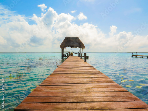 Turquoise waters in Laguna Bacalar, Quintana Roo, Mexico. Wooden walkway over crystal clear waters. Log cabin. Copy space photography