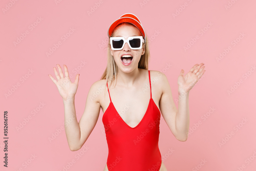 Shocked young blonde woman in red one-piece swimsuit cap eyeglasses isolated on pink background. People summer vacation rest lifestyle concept. Mock up copy space. Keeping mouth open, spreading hands. Shocked young blonde woman in red one-piece swimsuit cap eyeglasses isolated on pink background. People summer vacation rest lifestyle concept. Mock up copy space. Keeping mouth open, spreading hands.