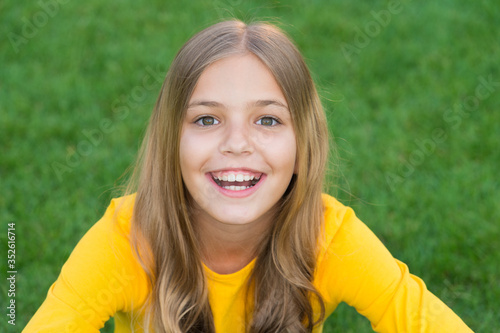 Pure beauty. little girl with pleasant smile. kid with cute curly hair. little beauty after visit hairdresser. fashion and beauty. happy childrens day. spring holiday. carefree child on green grass