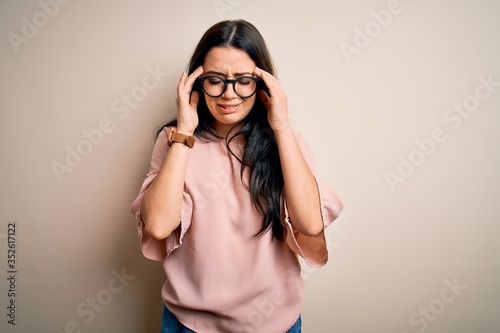 Young brunette elegant woman wearing glasses over isolated background with hand on head for pain in head because stress. Suffering migraine.