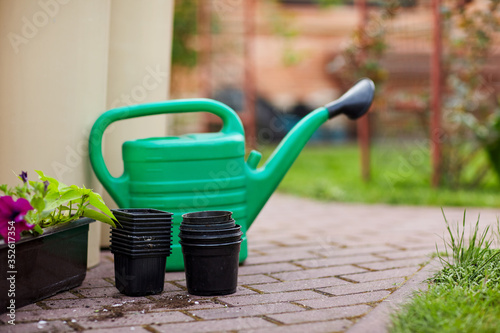 A green watering can, planting pots and a container of flowers are on the path in the garden