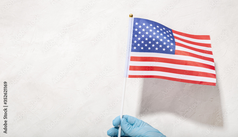 Obraz premium Hand in protecting glove holding American Flag Against White textured background. 4th of July concept. Copy space