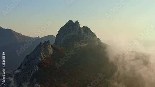 aerial survey of the mountain peak with overgrown forest and creeping mist slopes in the sunset