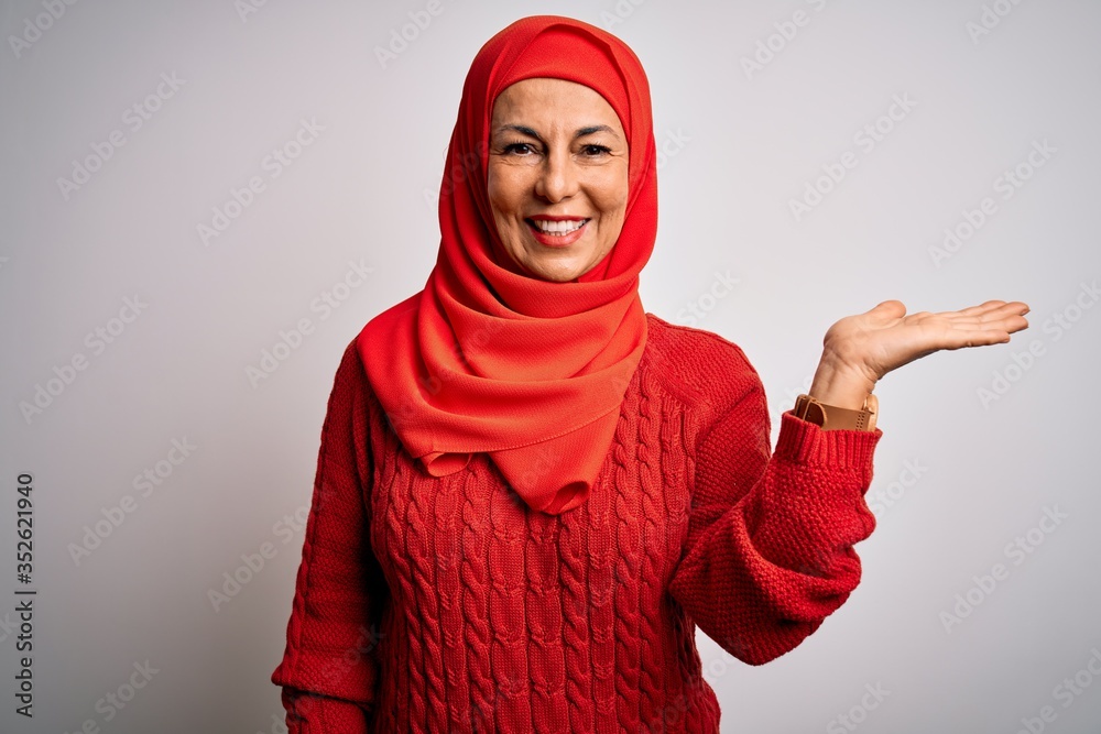 Middle age brunette woman wearing muslim traditional hijab over isolated white background smiling cheerful presenting and pointing with palm of hand looking at the camera. Middle age brunette woman wearing muslim traditional hijab over isolated white background smiling cheerful presenting and pointing with palm of hand looking at the camera.