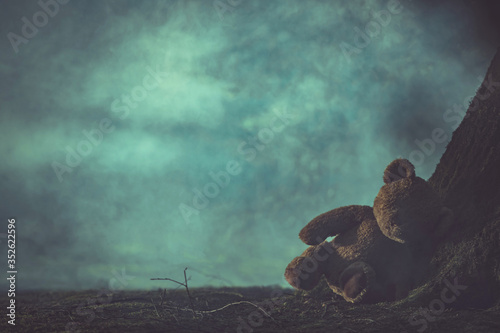 Child Abuse Concept with Lost Teddy Bear in Dark Foggy Forest.
