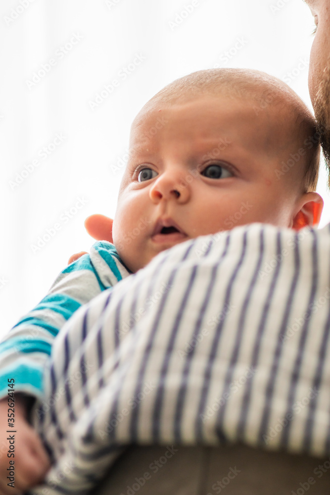 Little baby boy with reflux problem burps and spits in his father's arms, with cotton cloth on father's shoulder. Common baby feeding problem.