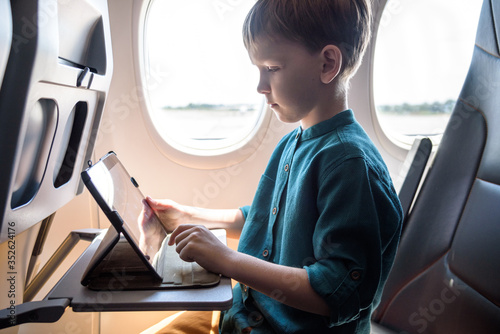 Cute six years old boy, playing on tablen in aircraft on boar, traveling on vacation with parents and siblings photo