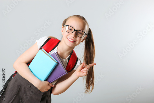Portrait of a cheerful schoolgirl with a backpack and stationery on a light background. Place for text. Back to school. Preparations for school.National School Backpack Awareness Day