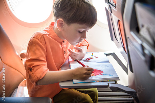 Charming kid traveling by an airplane. Joyful little boy sitting by aircraft window during the flight. Air travel with little kids