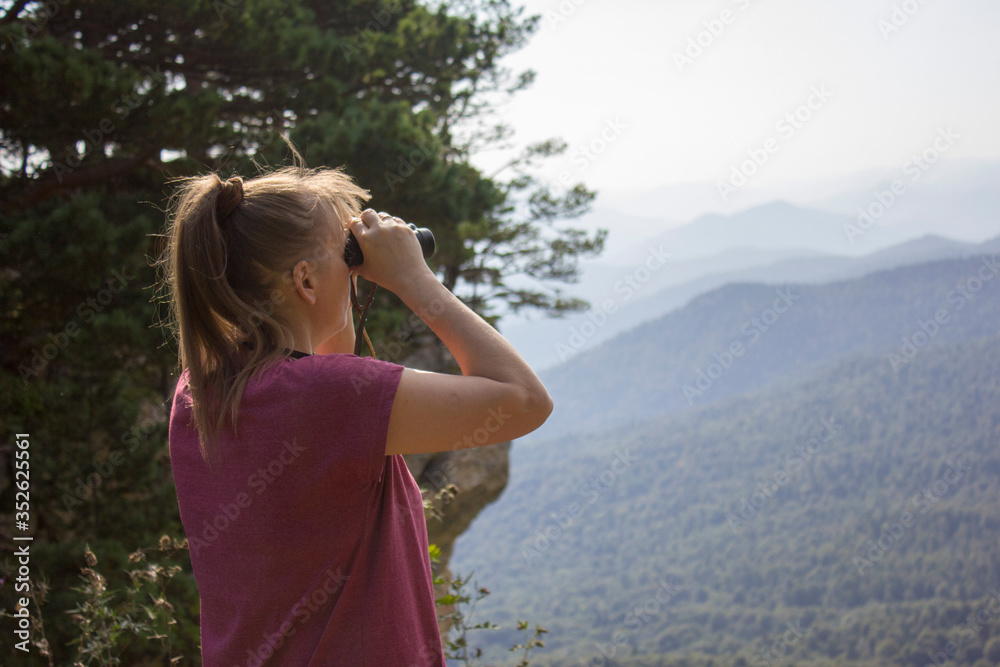 a girl on the edge of a mountain looks into the distance with binoculars a girl on the edge of a mountain looks into the distance with binoculars