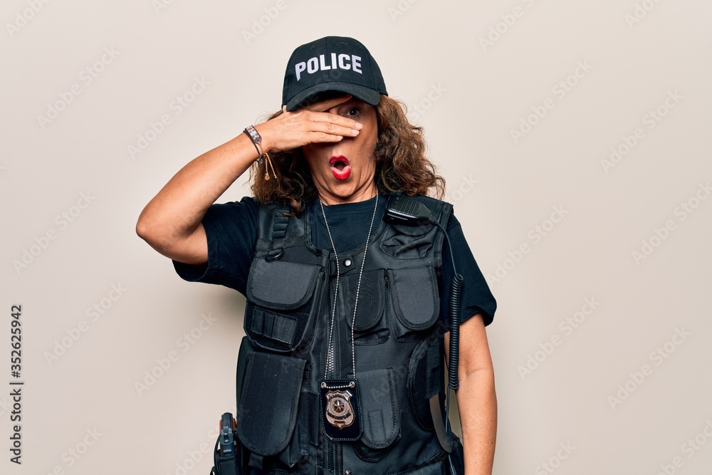 Middle age beautiful policewoman wearing bulletproof uniform and cap over white background peeking in shock covering face and eyes with hand, looking through fingers afraid Middle age beautiful policewoman wearing bulletproof uniform and cap over white background peeking in shock covering face and eyes with hand, looking through fingers afraid