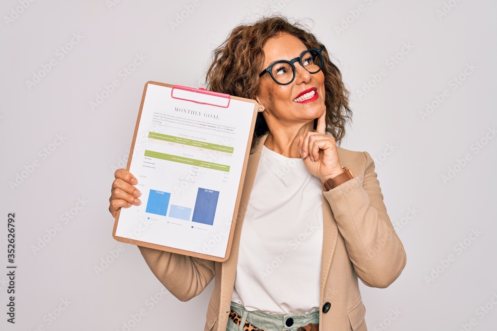 Middle age senior business woman holding monthly goal graphic on clipboard serious face thinking about question, very confused idea Middle age senior business woman holding monthly goal graphic on clipboard serious face thinking about question, very confused idea