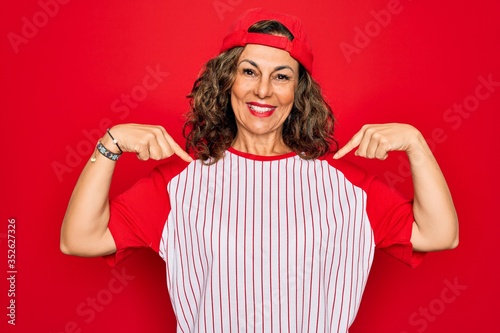 Photography Middle age senior woman wearing baseball equiment over red isolated background looking confident with smile on face, pointing oneself with fingers proud and happy