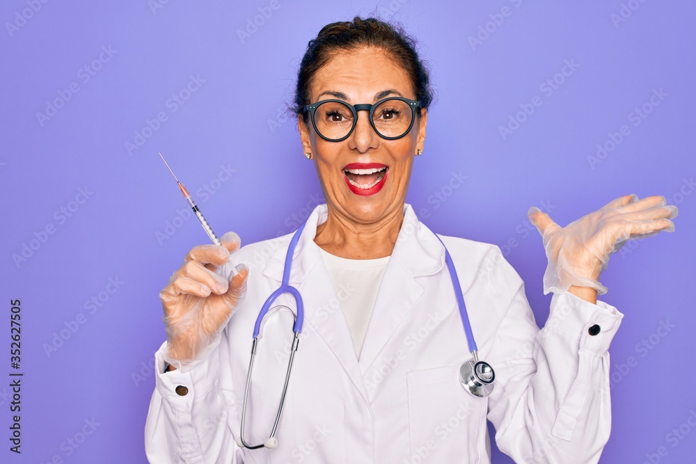 Middle age senior professional doctor woman holding syringe with medical vaccine very happy and excited, winner expression celebrating victory screaming with big smile and raised hands Middle age senior professional doctor woman holding syringe with medical vaccine very happy and excited, winner expression celebrating victory screaming with big smile and raised hands