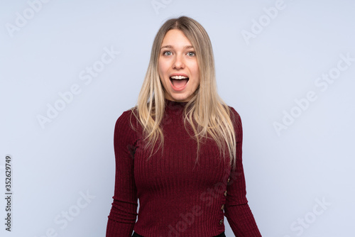 Young blonde woman over isolated blue background with surprise facial expression