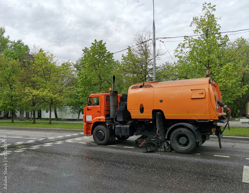 Orange sweeper machine (street sweeper) cleans city road.