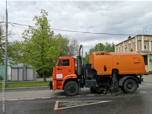 Orange sweeper machine (street sweeper) cleans city road.