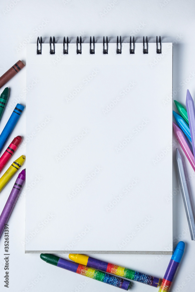 Background for an inscription. A white notebook and many colored pencils around it. Photo on a white background. Photo above Background for an inscription. A white notebook and many colored pencils around it. Photo on a white background. Photo above