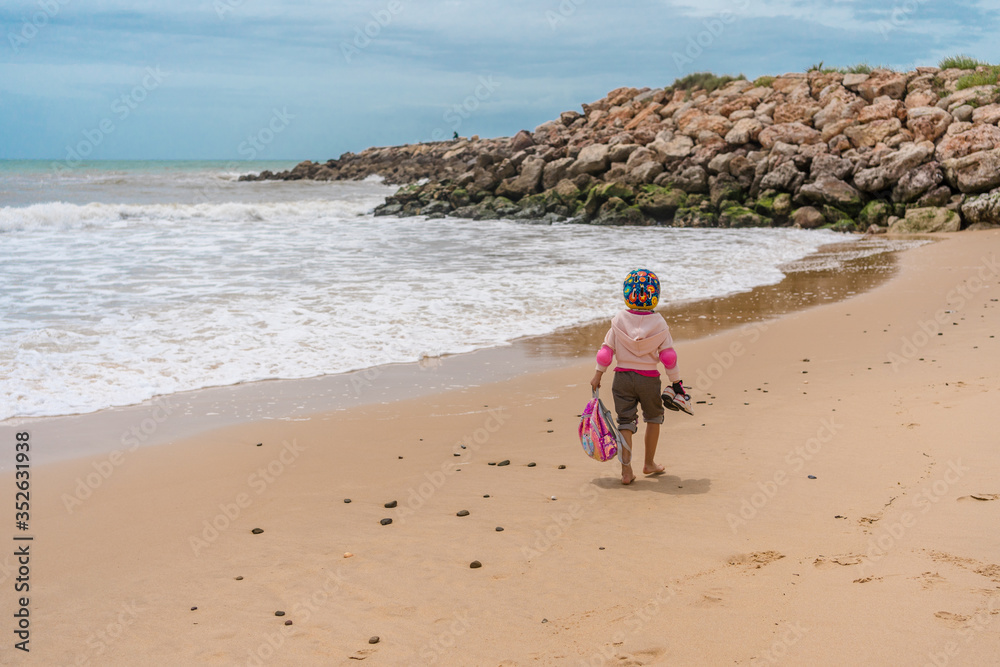 Back view of little girl walking on seafront sandy beach nature, cloudy sky weather outdoors background. Back view of little girl walking on seafront sandy beach nature, cloudy sky weather outdoors background.
