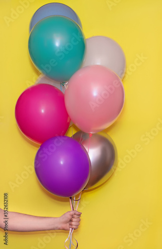 Hand holding colorful helium balloons isolated on yellow background!Holiday concept
