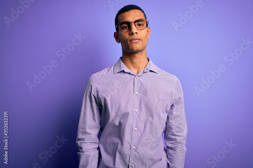 Handsome african american man wearing striped shirt and glasses over purple background looking sleepy and tired, exhausted for fatigue and hangover, lazy eyes in the morning. © Krakenimages.com